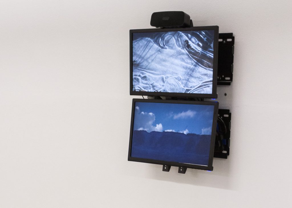 Two flat-screen monitors hanging on a white wall, arranged one above the other.